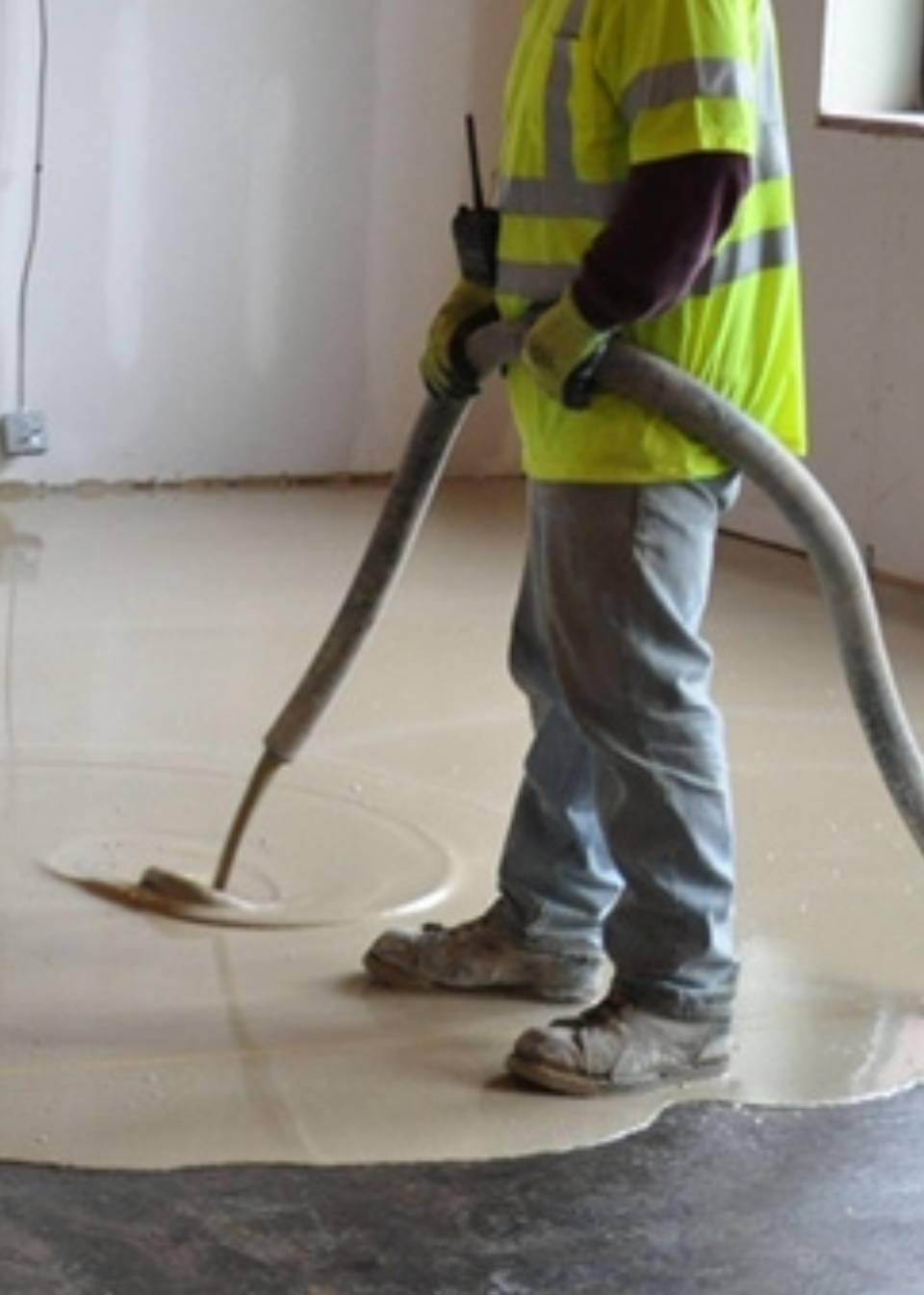 A person in yellow vest holding hose on floor.